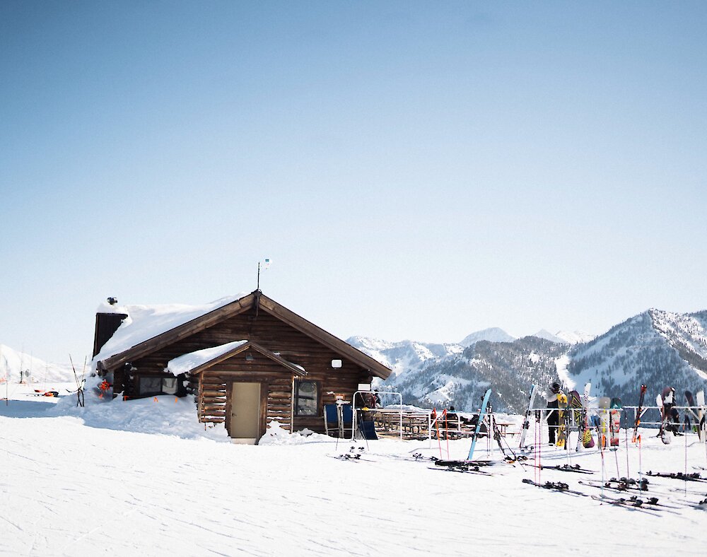 Bearclaw cabin buried in snow. A blue sky is shining down on skis scatted across the snow.