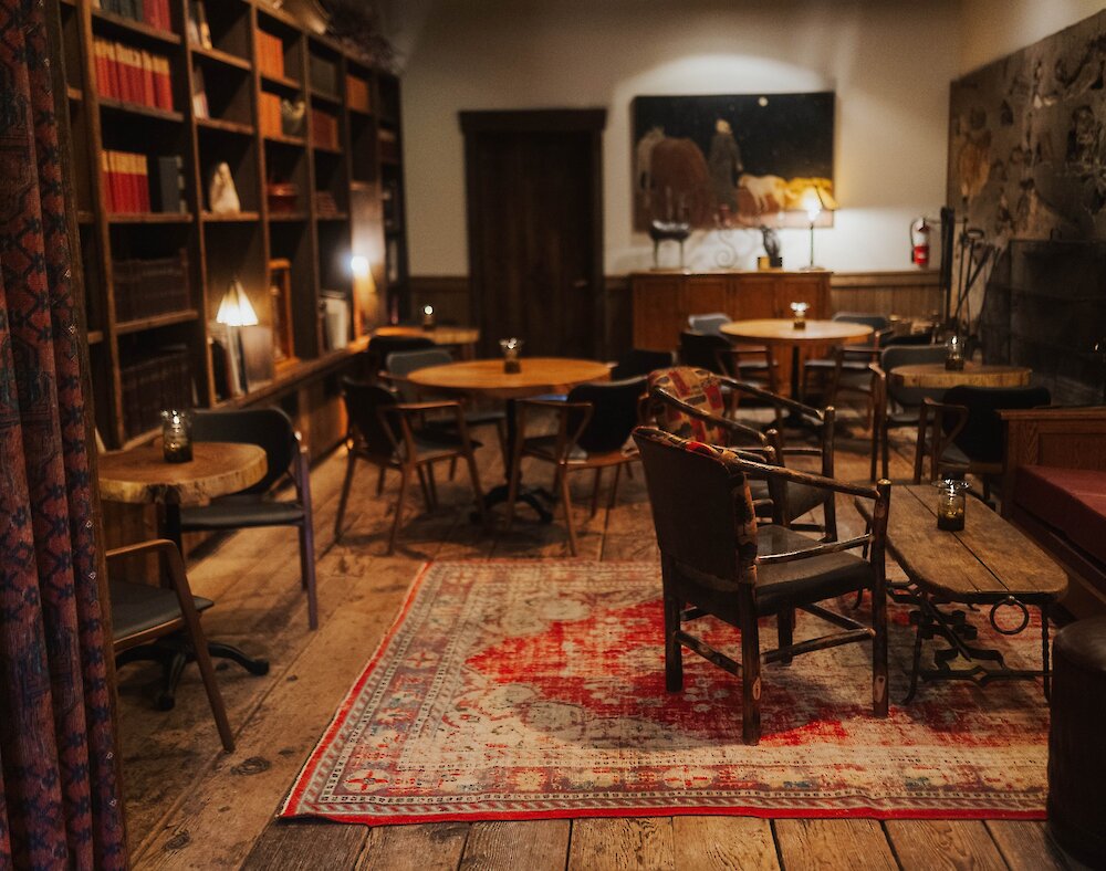 Warm room with tables, chairs, a red couch, book shelf, and fire place.