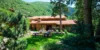 A spacious wooden house at Sundance Resort Venues with a large patio area featuring multiple tables, surrounded by lush green trees and a hilly landscape in the background.