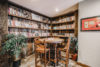 A cozy home library nook with a circular wooden table and chairs, surrounded by wall-to-floor bookshelves filled with books. decor includes plants and framed artwork.