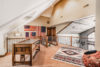 Spacious, sunlit attic room featuring exposed wooden beams, slanted ceilings, and a collection of historical american flags. an antique desk and a southwestern-style rug add character to the decor.