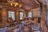 Cozy rustic cabin interior with log walls and wooden furniture, including a rocking chair and a sofa with cushions. soft lighting and fur rugs add warmth to the room.