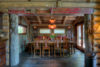 Rustic dining room with wooden furniture and decor, featuring carved totem-like figures beside the windows, antlers above the window, and a vibrant floral centerpiece on the dining table.