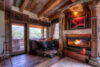 A rustic bathroom interior with a burning fireplace, a freestanding bathtub, wooden beams on the ceiling, and a scenic view seen through the open door.