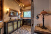Rustic bathroom interior featuring a decorative sink, ornate mirror, patterned tile floor, and vintage furnishings, with natural light streaming through a window.