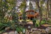 A picturesque wooden cabin nestled among lush trees in a serene forest setting, featuring large windows and a rocky garden path leading up to the house.