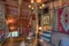Cozy log cabin interior featuring rustic wooden beams, a plush sofa with fur and pillows, a southwestern-style rug, and warm lighting from a chandelier and lamps. a portrait hangs on the wall.