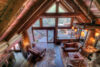Cozy, rustic cabin interior with high ceilings, large windows, and wooden beams. features plush seating, a fur rug, and a warm, inviting decor overlooking a forest.
