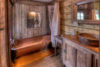 Rustic bathroom interior with a copper bathtub, wooden cabinetry, and a mirror. natural light streams in through a window, highlighting the vintage charm.