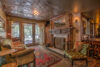 An opulent vintage living room with ornate wooden furniture, a decorative silver ceiling, plush green velvet armchairs, and a warm fireplace. refined curtains frame french doors leading to a garden.