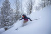 Woman smiles as she makes her way down the mountain on skis, with snow spraying behind her.