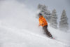 An individual snowboards down the mountain, with snow spraying behind them.