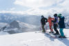A group of skiers gathers to chat at the top of the mountain with a stunning view of the snowy peaks.