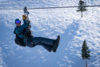 A man in winter gear zip-lines across the snow covered mountains.