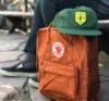An orange Fjallraven backpack with a forest green and yellow Sundance hat.