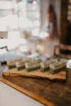 Handmade green soaps garnished with dried herbs, displayed on a wooden plank in a cozy, warmly lit art studio.