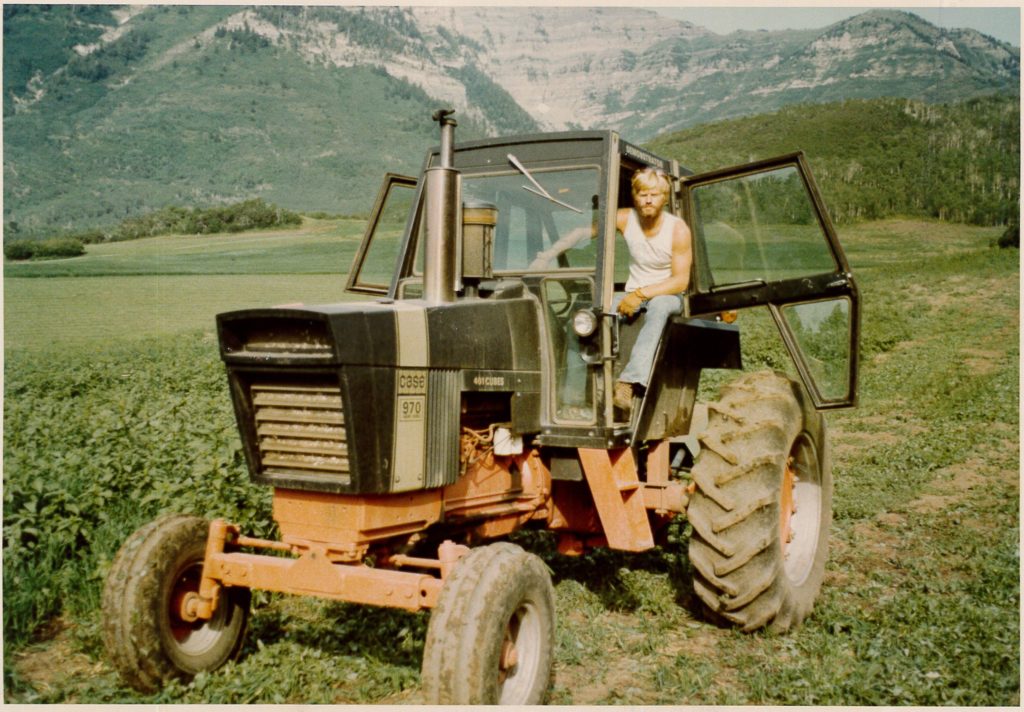 An old photo of young Robert Redford leaning out of a tractor.