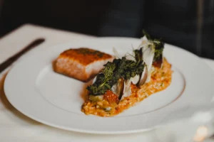 A gourmet salmon dish on a white plate, topped with herbs and served over a bed of risotto with tomato sauce, presented elegantly in a fine dining setting reminiscent of the best restaurants in Park City