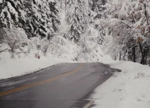 A mountain road surrounded by a snow covered forest on either side.