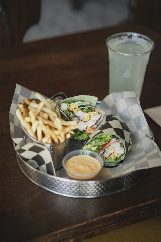 Colorful lunch wrap with chicken and a variety of vegetables, served with fries and a drink.