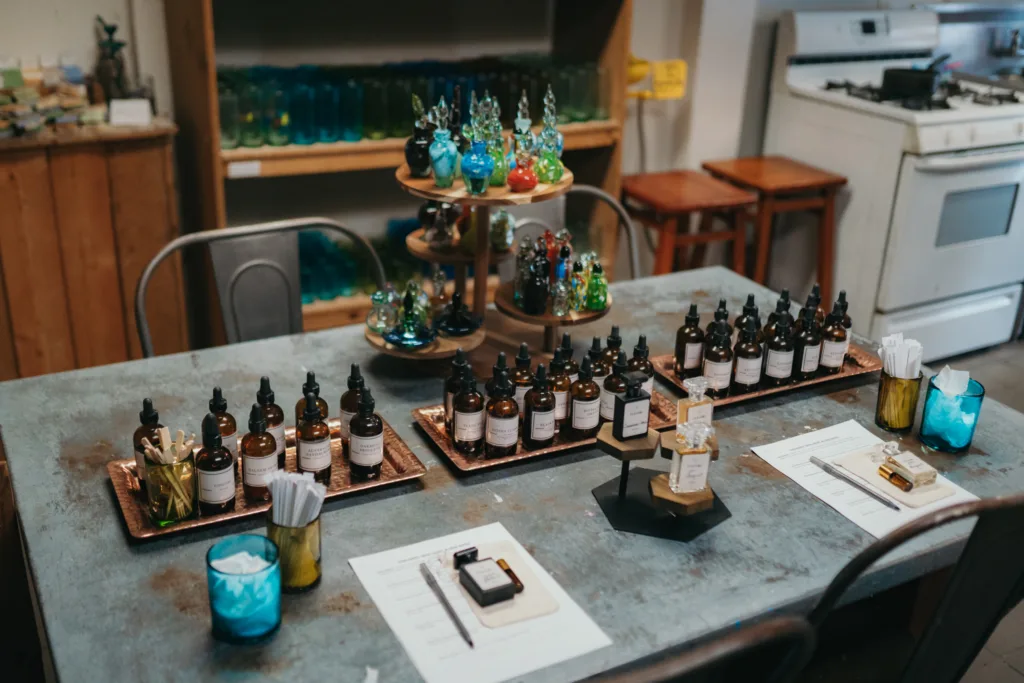 A cozy artisanal shop displaying various glass bottles and jars on wooden tables, with shelves of colorful glassware in the background.