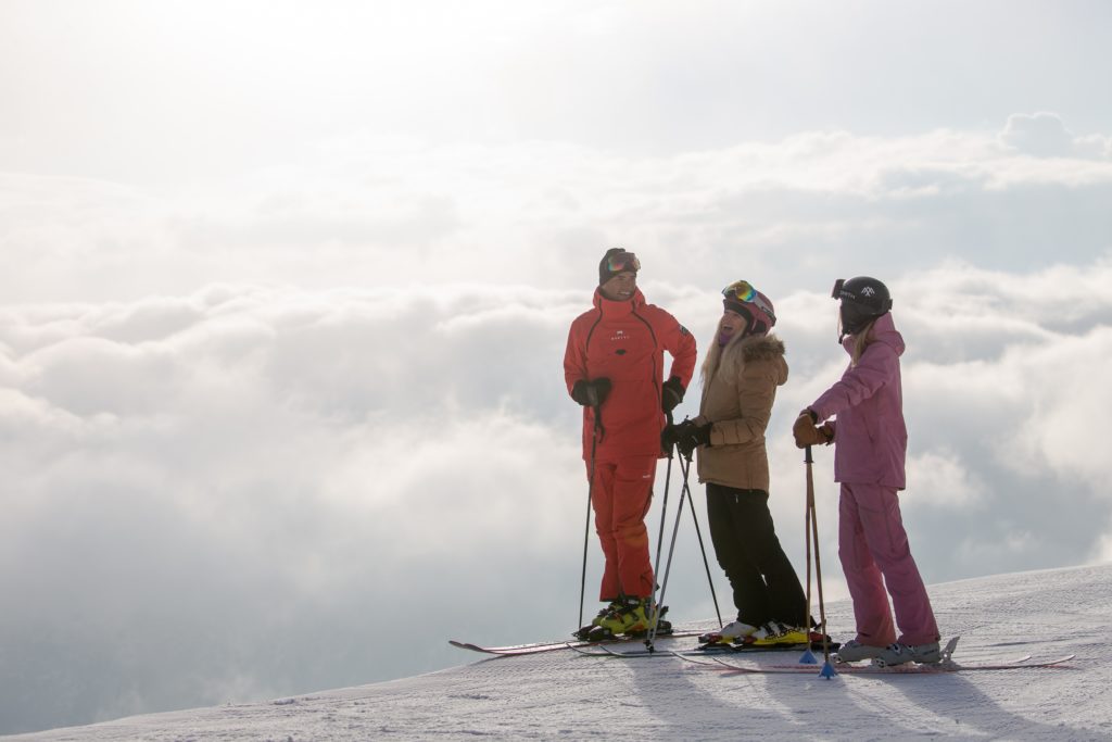 Three skiers at the top of the mountain on a cloudy day. 