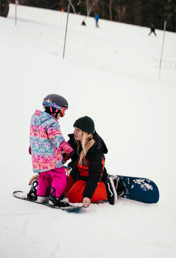 A Sundance Resort ski instructor teaching a young child how to snowboard. 