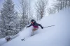 Woman smiles as she makes her way down the mountain on skis, with snow spraying behind her.