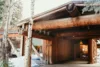 A rustic wooden cabin surrounded by snow-covered trees, featuring a robust, log-based construction with a welcoming, illuminated entrance.