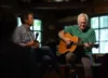 Two men on stage perform a musical number with a guitar.