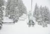 A snowy scene with skiers riding a chairlift ascending through frost-covered trees, visibility reduced by heavy snowfall.