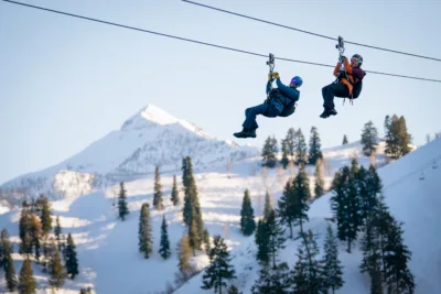 Two people riding the zipline through the snowy mountains.