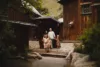 A family of four stands in front of a rustic cabin surrounded by lush greenery. two adults and two children smile as they descend the wooden steps of their mountain retreat.