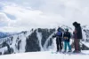 A family of skiers gathers to chat at the top of the mountain with a stunning view of the snowy peaks.