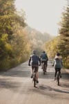 A group of bikers traveling up a paved mountain road with dense forest on either side.