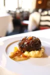 A succulent grilled steak served on a bed of creamy mashed potatoes with gravy, plated elegantly in a sophisticated restaurant setting.