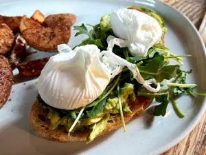 Avocado toast complete with leafy greens, eggs, and a side of seasoned potatoes.