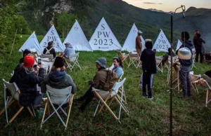 Group of people sitting on chairs around a campfire, with teepee-style tents marked 
