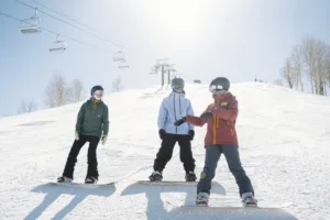 Sunny day on the slopes with two new snowboarders listening to their instructor.