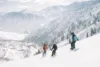 Two individuals learning how to snowboard with their instructor and a stunning mountain top view.