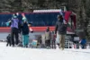 A family of skiers walking away from the ski lift holding all of their equipment.