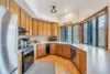 Spacious kitchen with wooden cabinets, stainless steel appliances, and a large countertop. A microwave and coffee maker sit on the counter. Large windows provide natural light, while a 