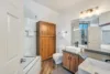 Modern bathroom with a wooden cabinet, glass-enclosed bathtub, and two white vessel sinks on a granite countertop. Two mirrors and wall-mounted lights evoke the soft glow of moonrise, while neatly folded towels on racks enhance the cozy ambiance created by warm wood and neutral tones.