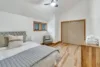 A minimalist bedroom showcases a bed with gray and white bedding under a cushioned headboard, evoking the calm of a moonrise. A wooden chair sits by closed double doors, while folded towels rest on a dresser. A ceiling fan and windows complete the serene space.