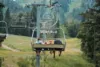 Three people sit on a chairlift suspended over a grassy, wooded hillside, heading up a mountain with empty chairs visible in the background—perfect terrain for nearby mountain horseback riding adventures.
